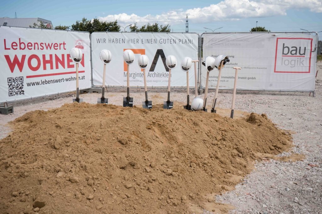 Spatenstich mit Bauhelmen und Schaufeln vor dem Bauprojektbanner