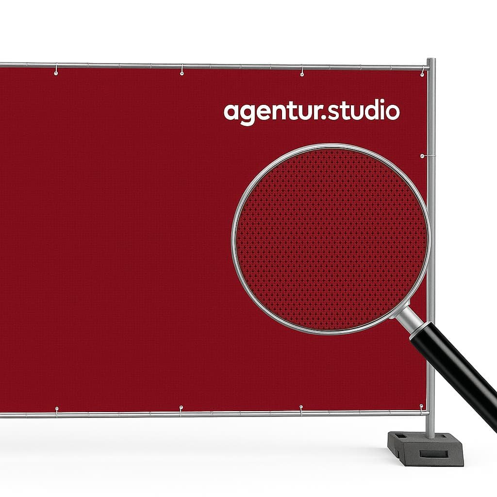 Bauzaunbanner aus Mesh-Gewebe in Dunkelrot mit weißem agentur.studio Logo, befestigt an Metallrahmen, Lupe zeigt die feine Mesh-Struktur im Detail.